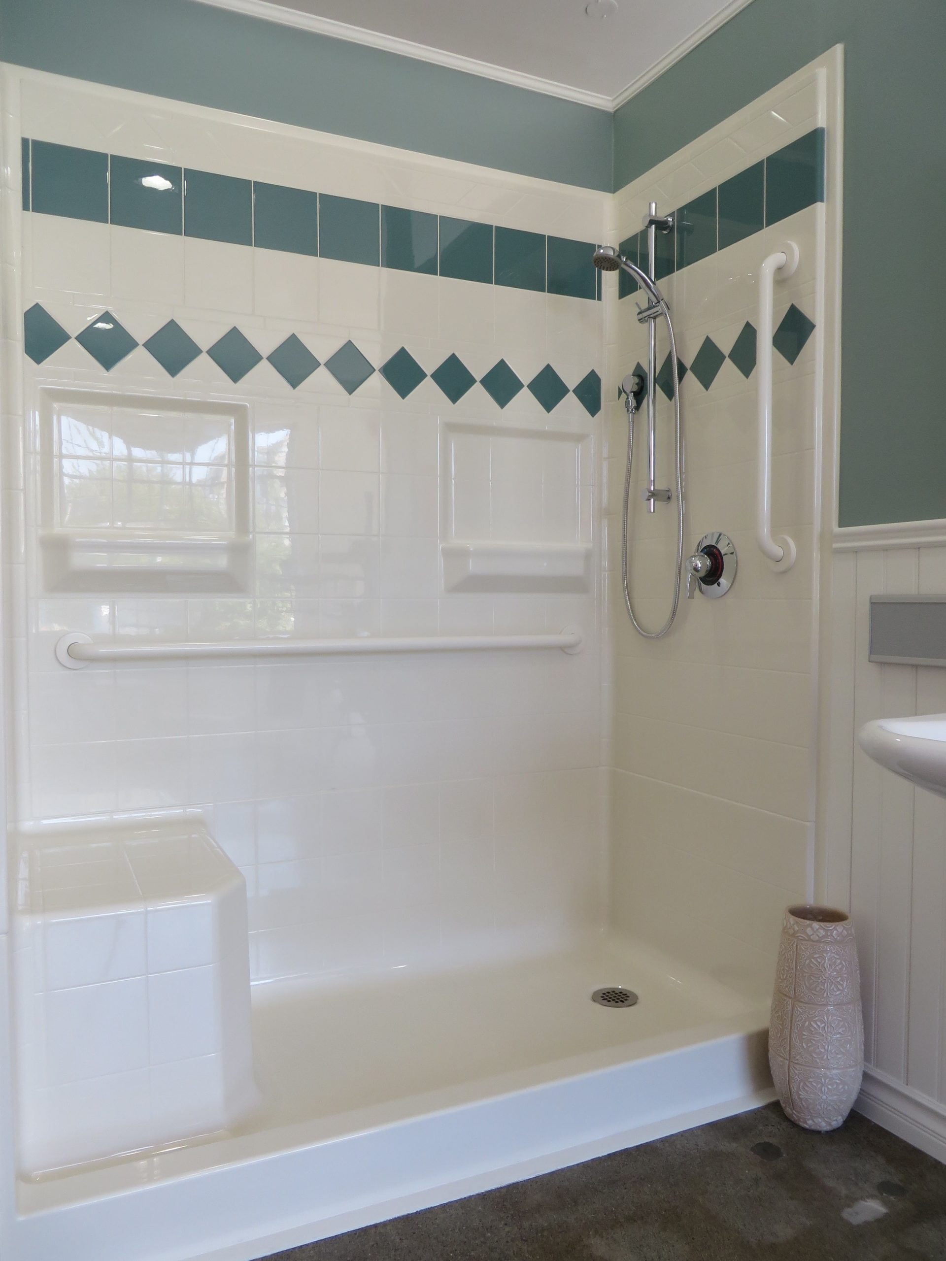 The 4LDSS6030 is a four-piece 60” x 30” curbed shower with a 5” threshold, end drain, built-in seat, grab bars, handheld showerhead, and teal accent tiles on white walls. A decorative vase stands outside the shower.