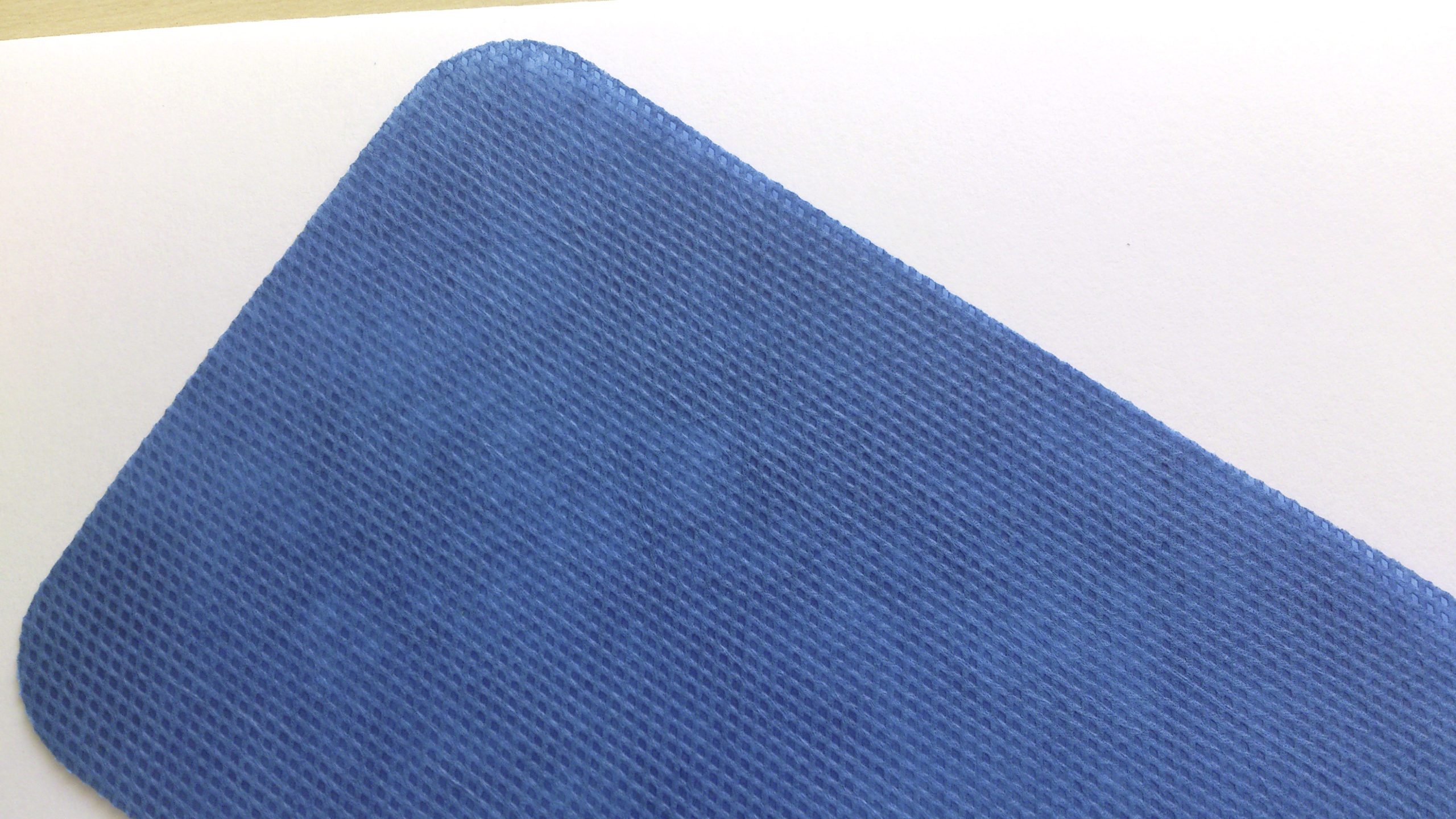 A close-up of a Zerøtex disposable curtain, featuring a blue textured surface and rounded corners, is placed on a white background, occupying the top left portion of the image.