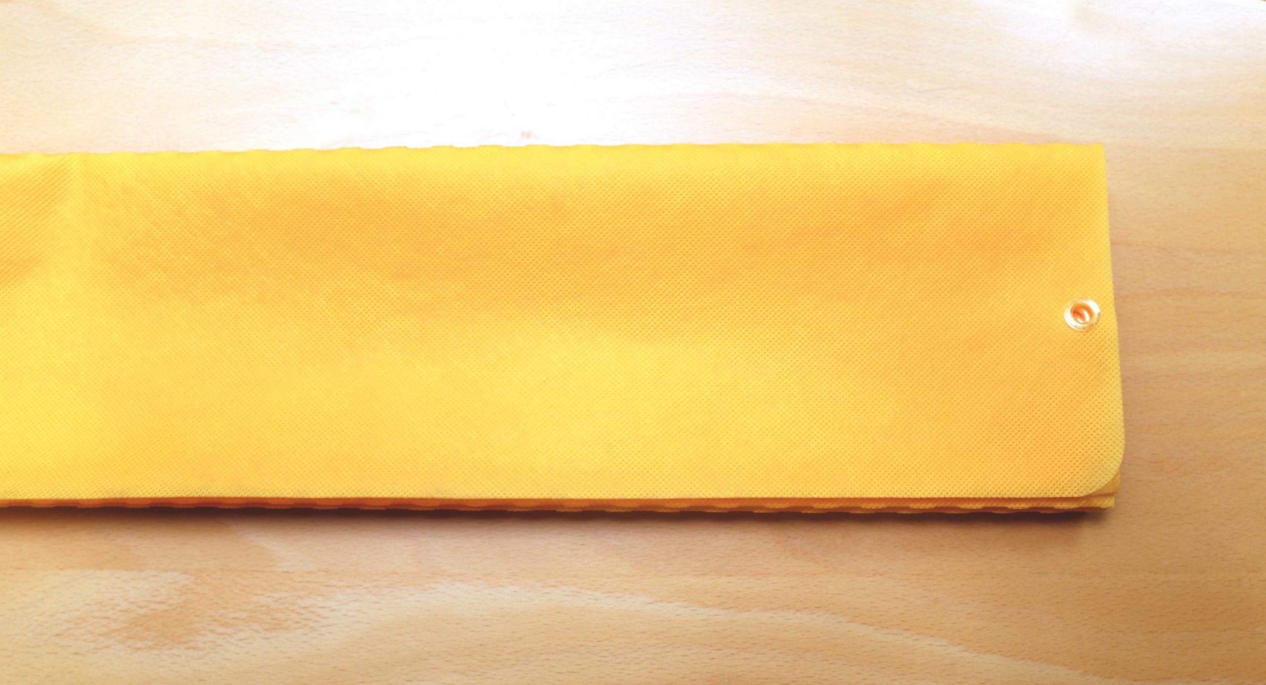 A Zerøtex disposable curtain in yellow, rectangular with a snap button closure, is displayed on a light wooden surface.